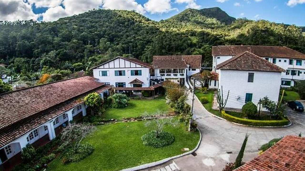 Fachada do Hotel Buscky, com edifícios brancos e telhados de telha, em meio à natureza.