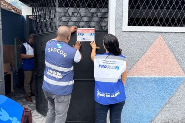 Fiscalização do Procon-RJ em estabelecimento, com sinalização de interdição. Agentes colam aviso na porta.