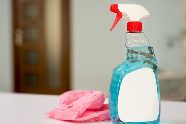 Frasco de produto de limpeza azul com borrifador, rótulo em branco e pano rosa