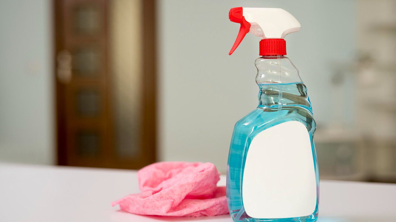 Frasco de produto de limpeza azul com borrifador, rótulo em branco e pano rosa