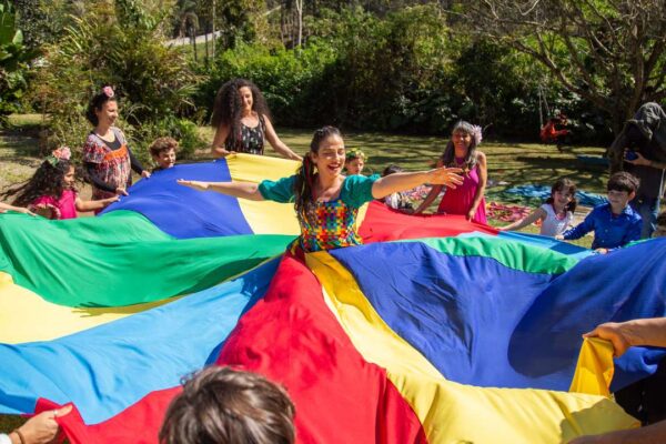 Grupo de pessoas brincando com um paraquedas colorido em atividade cultural ao ar livre.