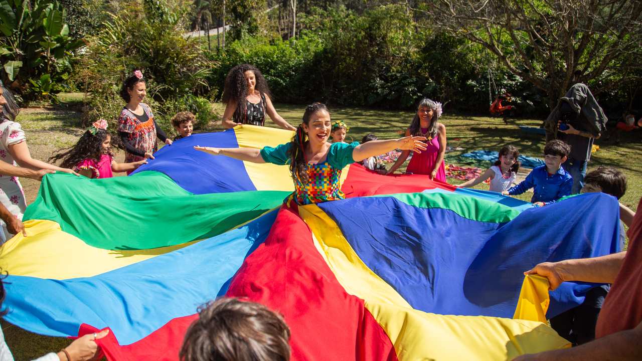 Grupo de pessoas brincando com um paraquedas colorido em atividade cultural ao ar livre.