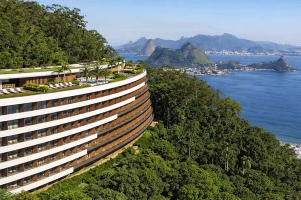 Hotel moderno em encosta com vista para o mar e montanhas.