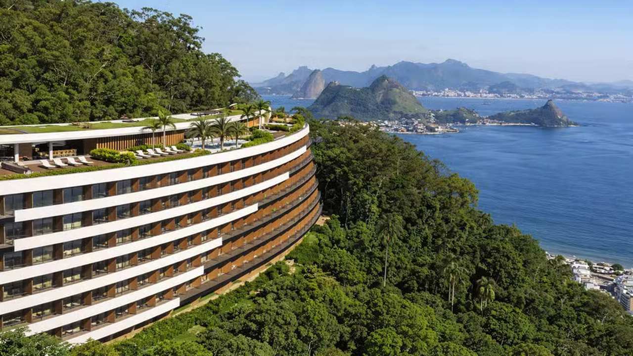 Hotel moderno em encosta com vista para o mar e montanhas.