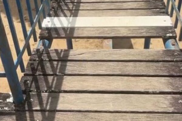 Imagem de ponte de madeira em parque infantil com brinquedos danificados.