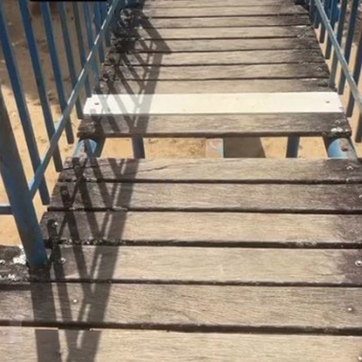 Imagem de ponte de madeira em parque infantil com brinquedos danificados.