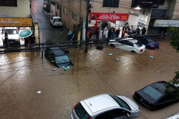 Inundação em rua com carros submersos e estabelecimentos comerciais.