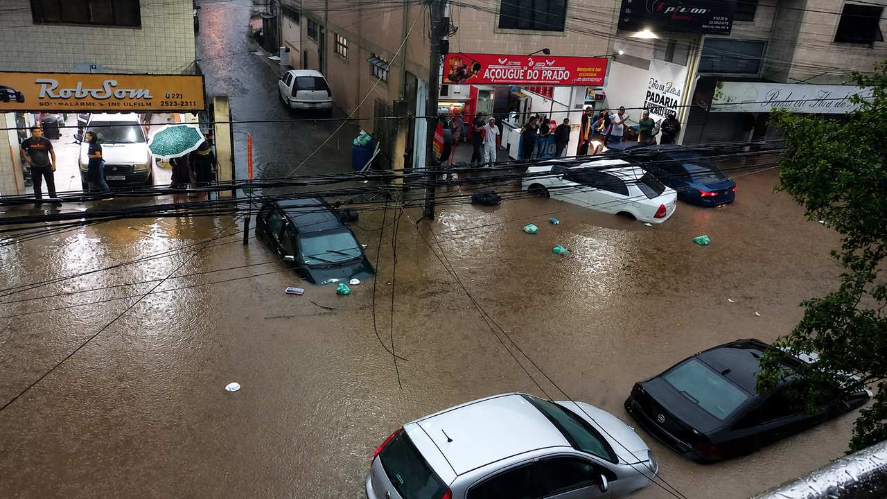Inundação em rua com carros submersos e estabelecimentos comerciais.