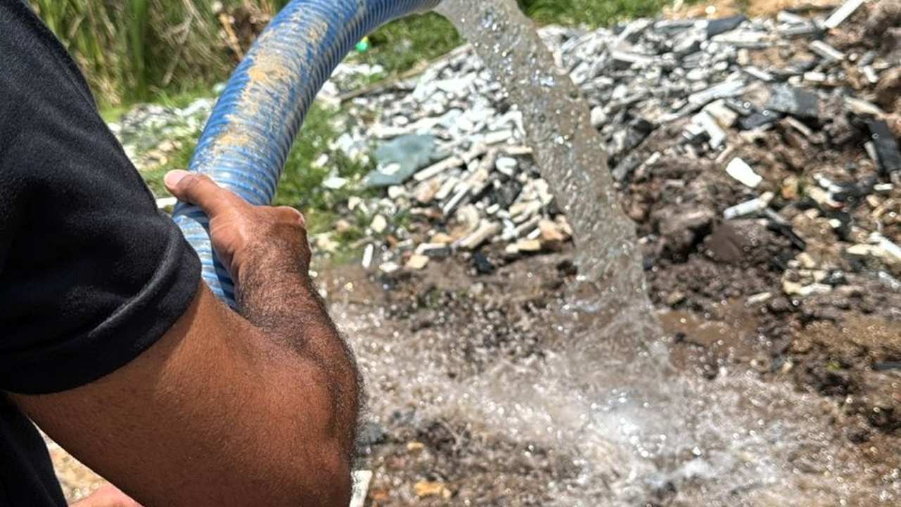 Mangueira de água sendo utilizada em área afetada por falta de abastecimento.