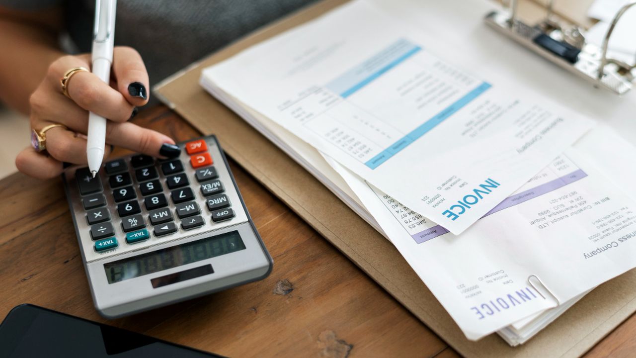 Mão com caneta e calculadora calculando fatura da concessionária.