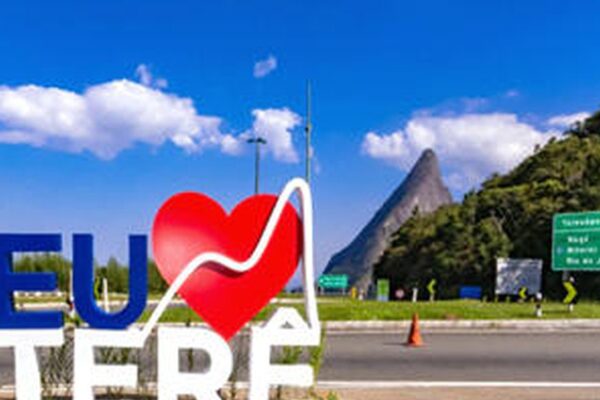 Marco turístico 'Eu Amo Teresópolis' com coração e vista da montanha Dedo de Deus sob céu azul.