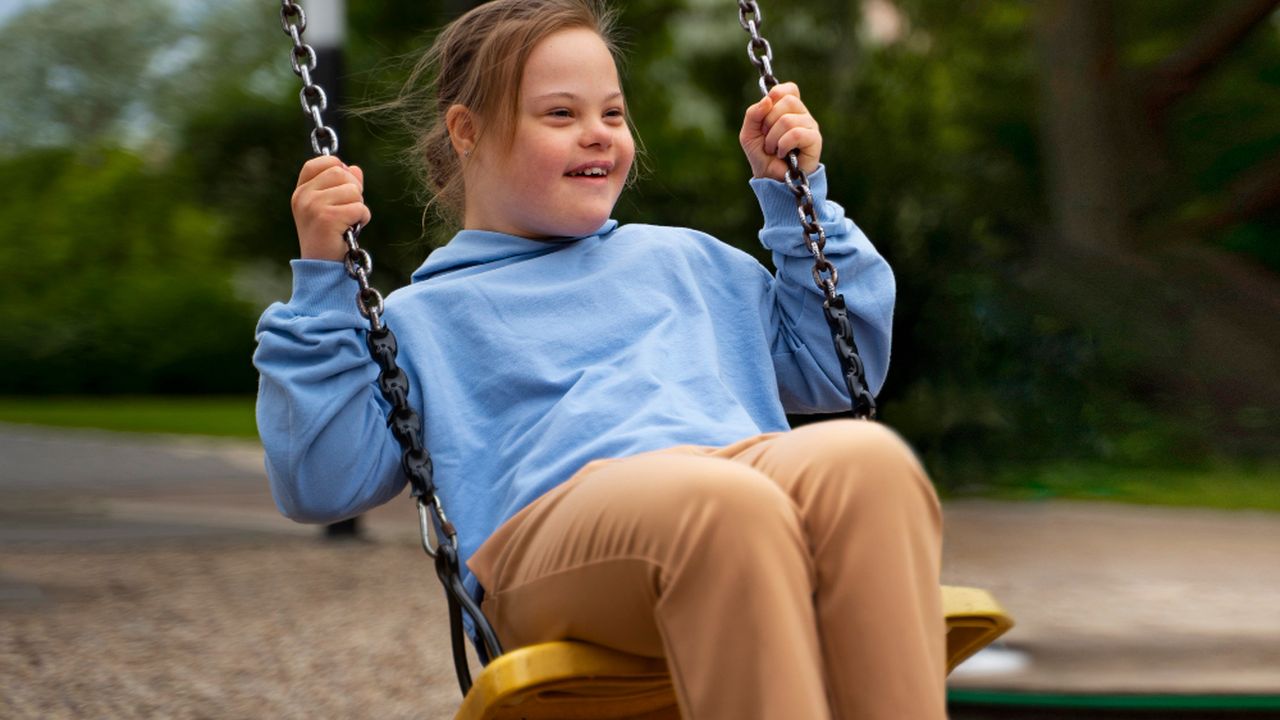 Menina com síndrome de Down se divertindo em um balanço em um parque, sorrindo