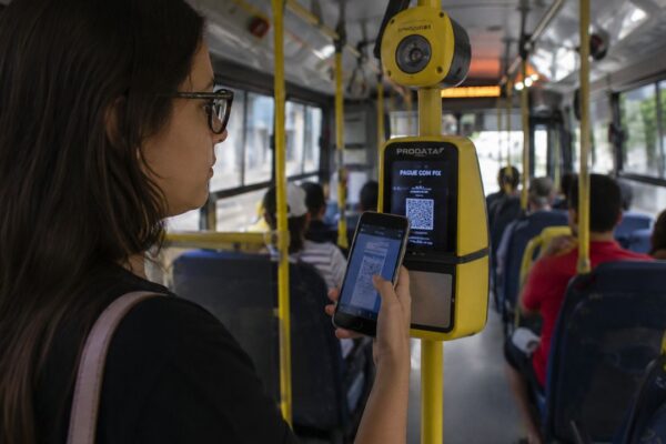 Mulher utilizando aplicativo para pagar passagem de ônibus com celular, no Brasil.