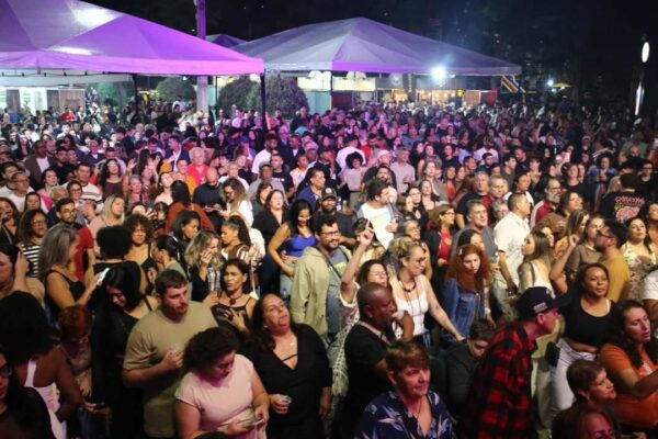 Multidão no evento Art & Bier na Praça do Suspiro, Nova Friburgo, com tendas e iluminação.