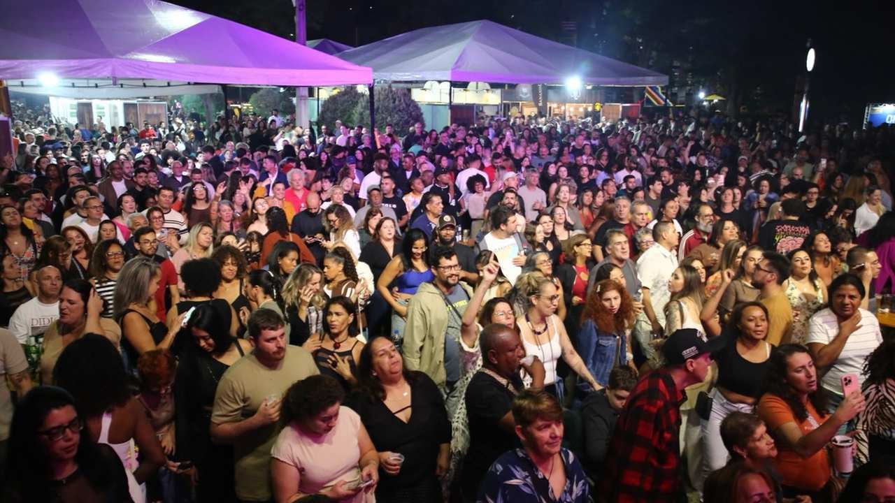 Multidão no evento Art & Bier na Praça do Suspiro, Nova Friburgo, com tendas e iluminação.