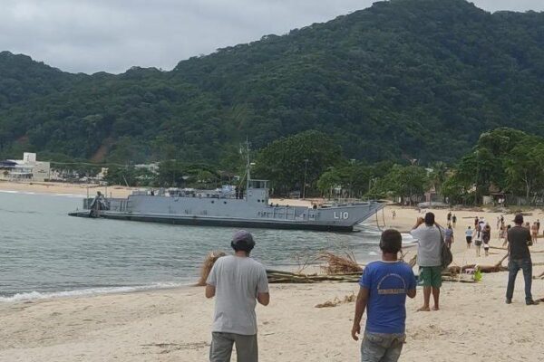 Navio da Marinha encalhado na Praia da Macumba, Rio de Janeiro. Pessoas na praia observam.