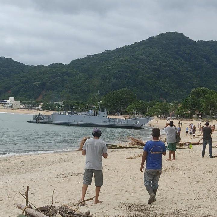 Navio da Marinha encalhado na Praia da Macumba, Rio de Janeiro. Pessoas na praia observam.