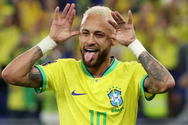 Neymar com a camisa do Brasil faz gesto engraçado, mostrando a língua e mãos perto das orelhas.