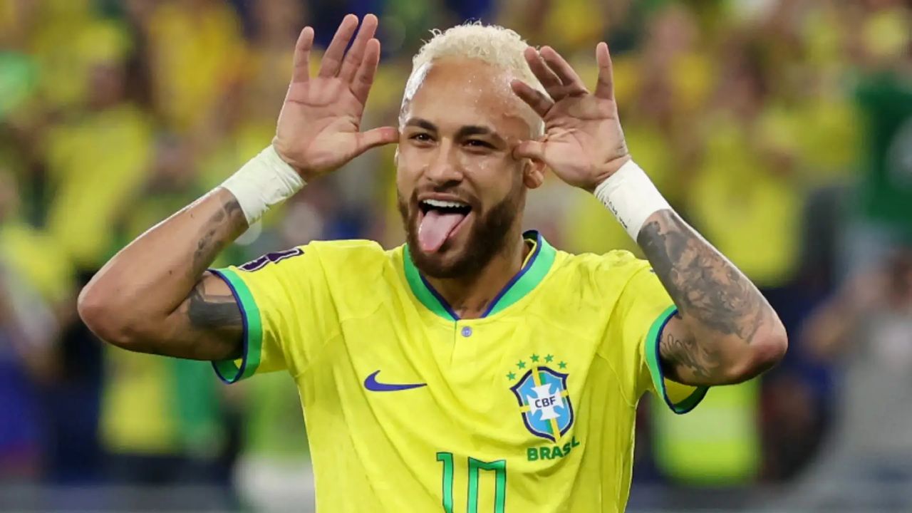 Neymar com a camisa do Brasil faz gesto engraçado, mostrando a língua e mãos perto das orelhas.