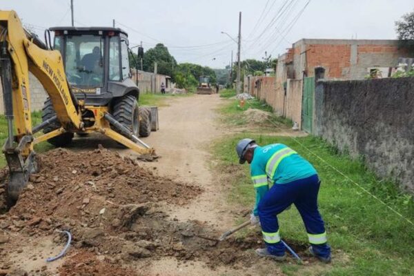Obra de saneamento com retroescavadeira e trabalhador cavando.