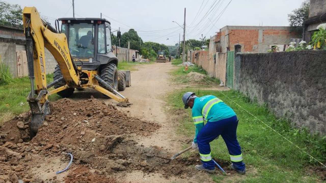 Obra de saneamento com retroescavadeira e trabalhador cavando.