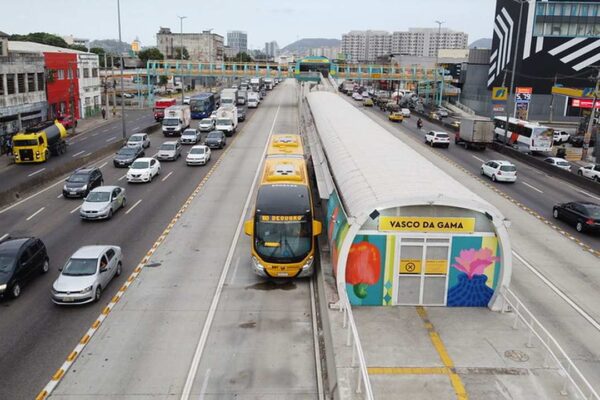 Ônibus BRT amarelo na estação Vasco da Gama no Rio de Janeiro, com trânsito intenso ao redor.