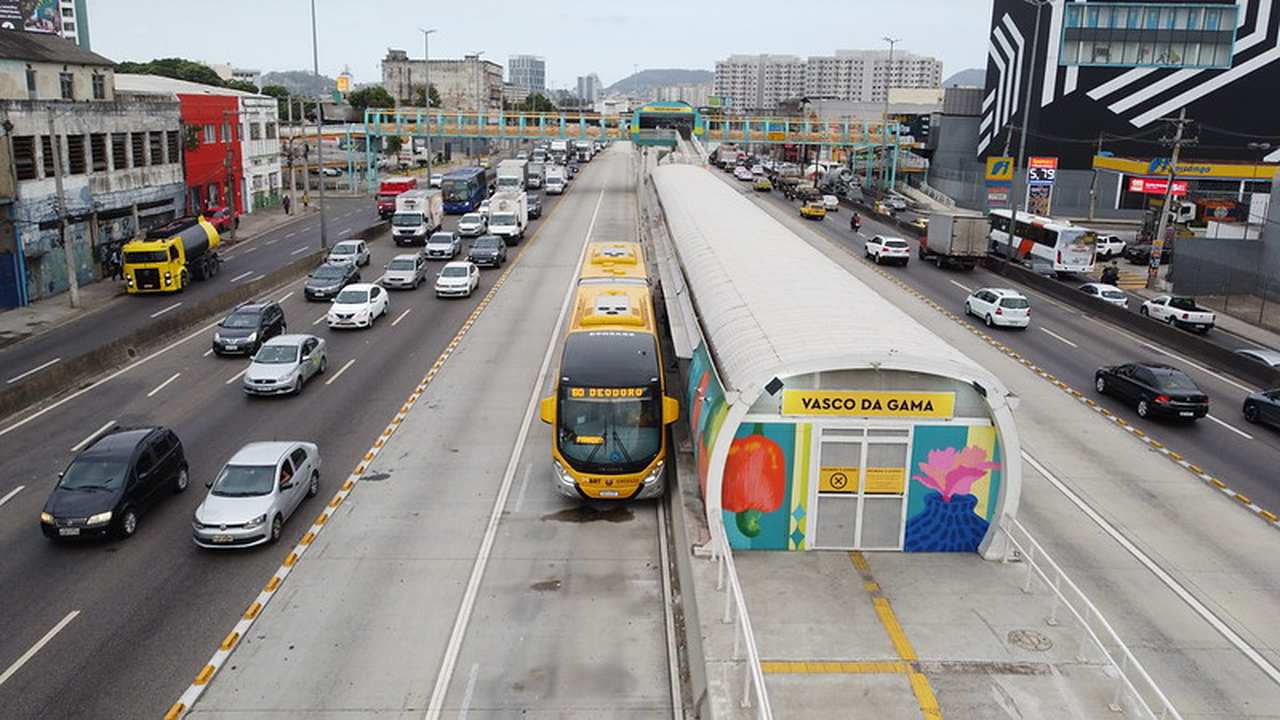 Ônibus BRT amarelo na estação Vasco da Gama no Rio de Janeiro, com trânsito intenso ao redor.