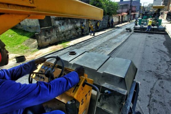 Operário dirigindo máquina em obra de pavimentação asfáltica em rua.