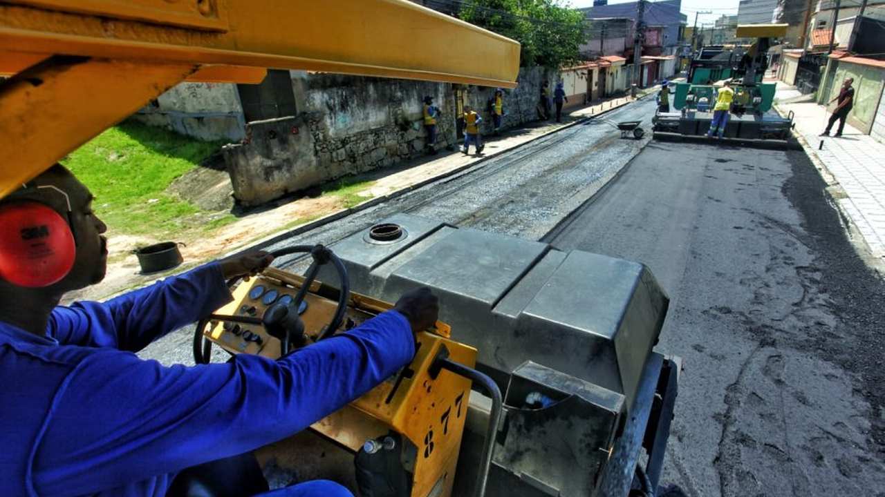 Operário dirigindo máquina em obra de pavimentação asfáltica em rua.