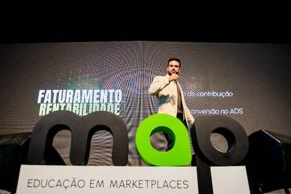Palestrante em evento de e-commerce em Nova Friburgo, com logos e tela de fundo.
