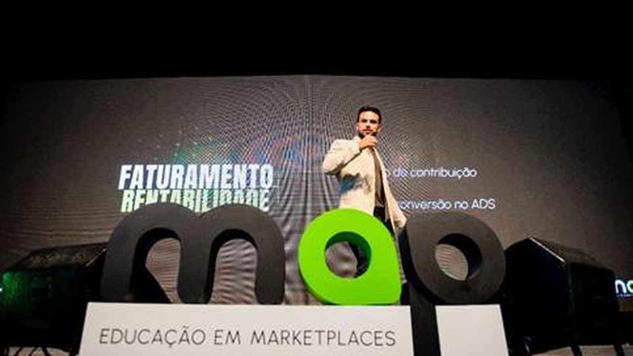 Palestrante em evento de e-commerce em Nova Friburgo, com logos e tela de fundo.
