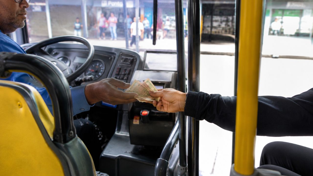 Passageiro pagando a passagem em dinheiro para o motorista de ônibus