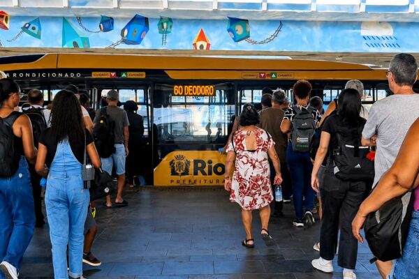 Passageiros aguardam ônibus em estação no Rio de Janeiro, com painel '60 Deodoro'.