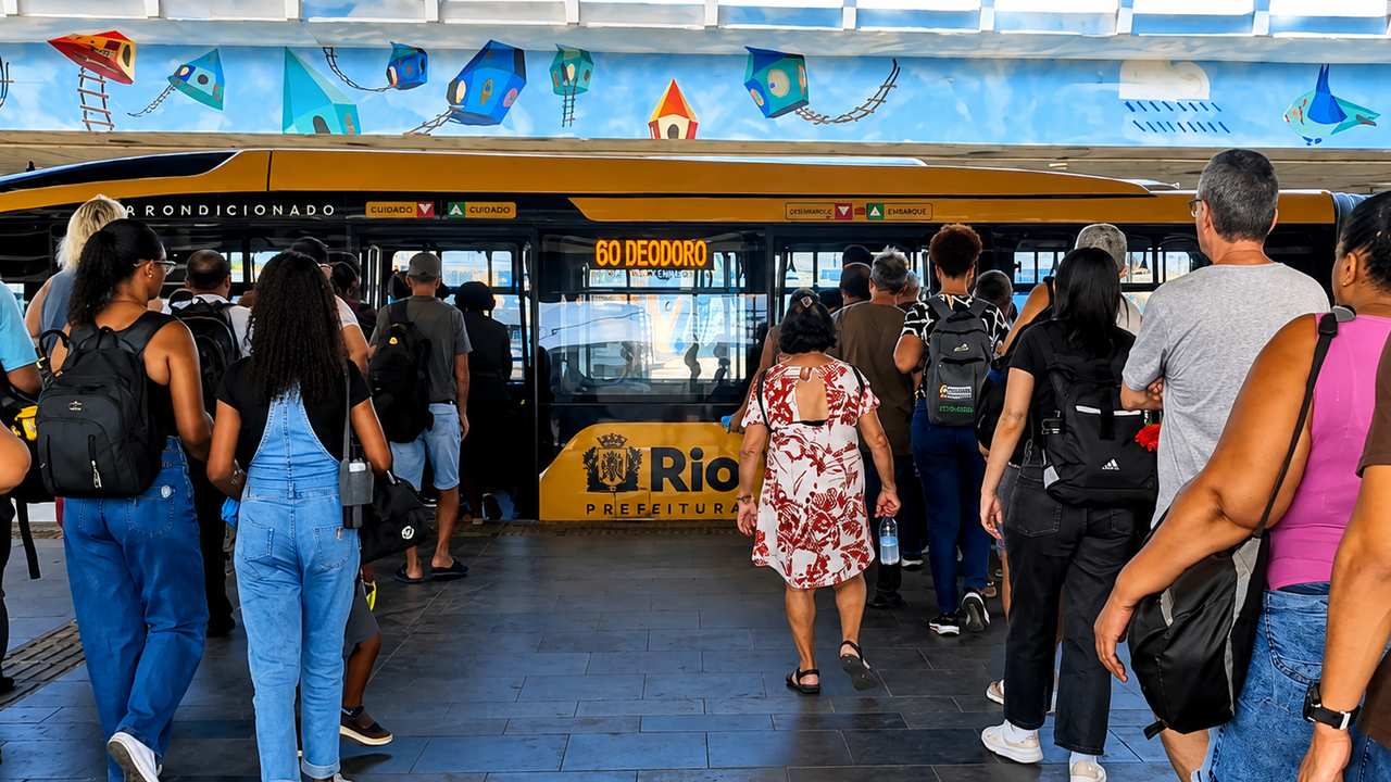 Passageiros aguardam ônibus em estação no Rio de Janeiro, com painel '60 Deodoro'.