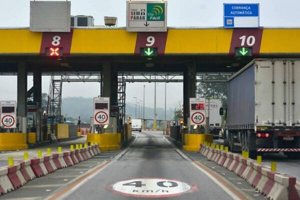 Pedágio com cancelas e sinalização, com destaque para a cobrança automática e velocidade limitada.