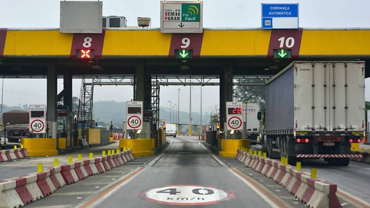Pedágio com cancelas e sinalização, com destaque para a cobrança automática e velocidade limitada.
