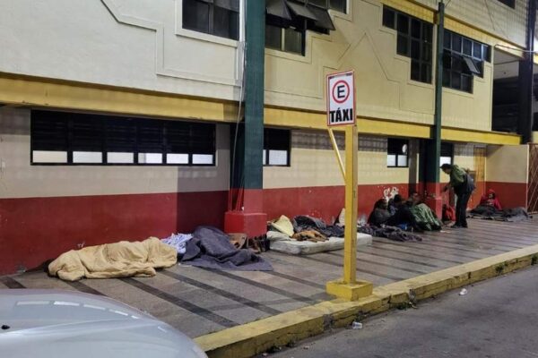 Pessoas em situação de rua em frente a um prédio, com cobertores e colchões.