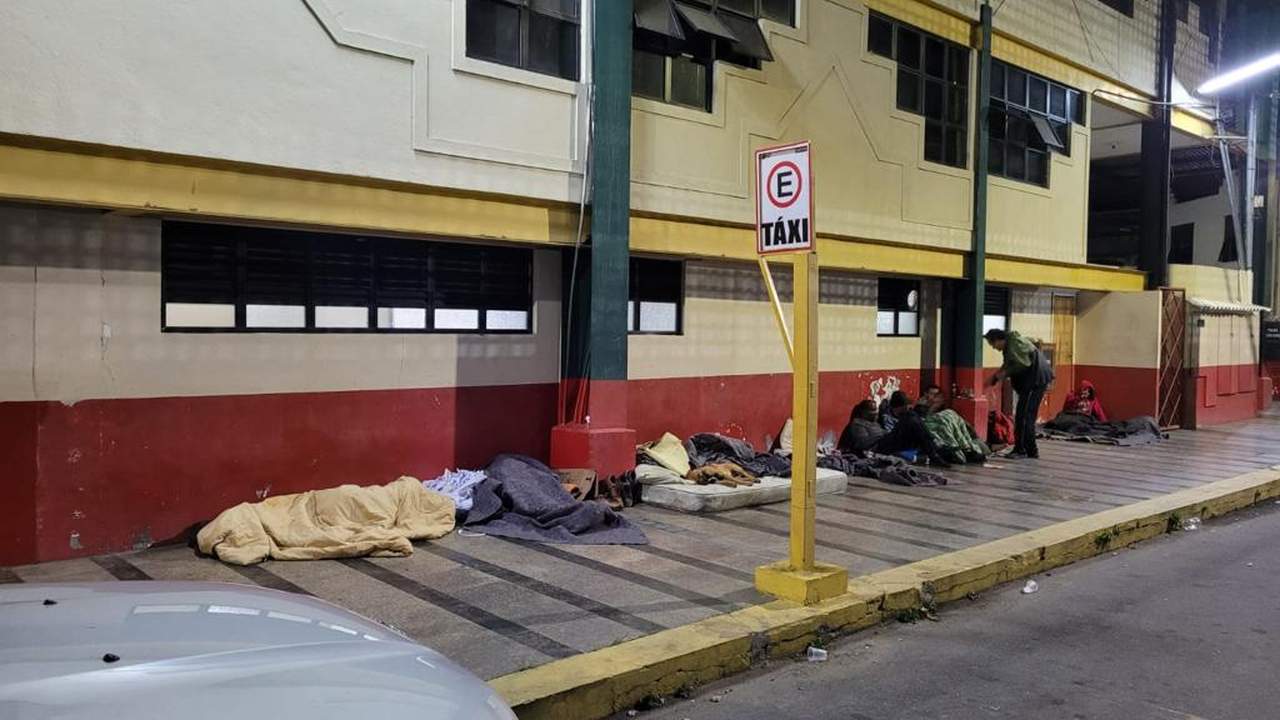 Pessoas em situação de rua em frente a um prédio, com cobertores e colchões.