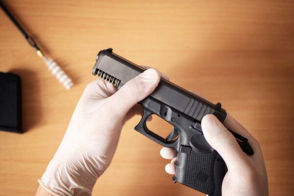 Pistola sendo manuseada com luvas, possivelmente em processo de limpeza ou manutenção.