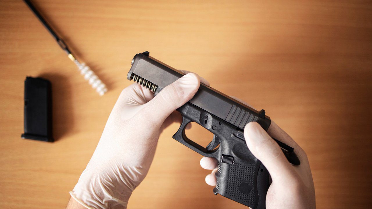 Pistola sendo manuseada com luvas, possivelmente em processo de limpeza ou manutenção.