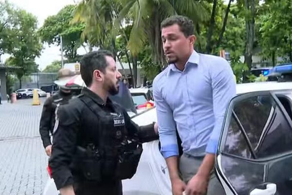 Policial conduz homem para viatura policial em investigação.