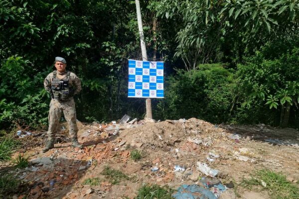 Policial militar em área de descarte irregular de entulho e resíduos de construção próximo a mata.