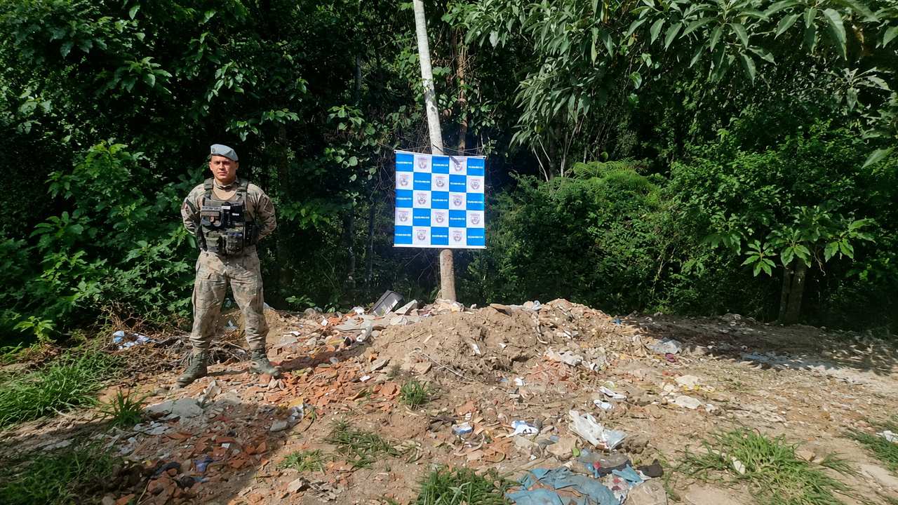 Policial militar em área de descarte irregular de entulho e resíduos de construção próximo a mata.