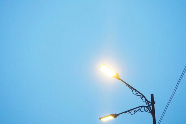 Postes de iluminação pública com luzes acesas contra céu azul.