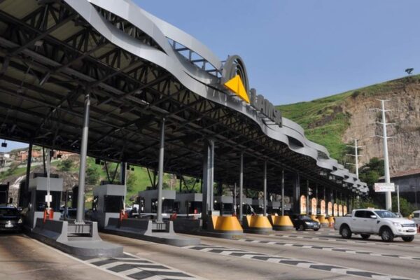Praça de pedágio em rodovia, com veículos passando e estrutura de cobertura.