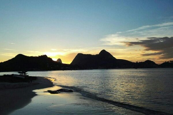 Praia de Charitas em Niterói ao pôr do sol, com montanhas ao fundo.