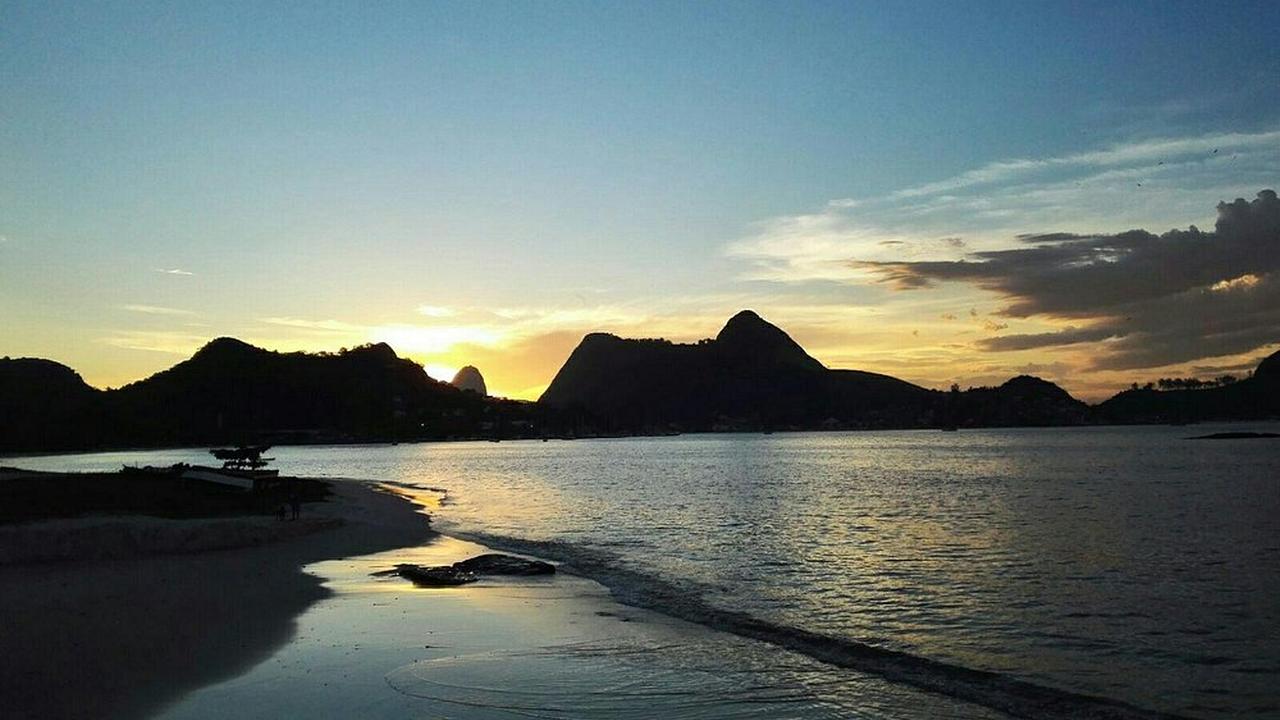 Praia de Charitas em Niterói ao pôr do sol, com montanhas ao fundo.