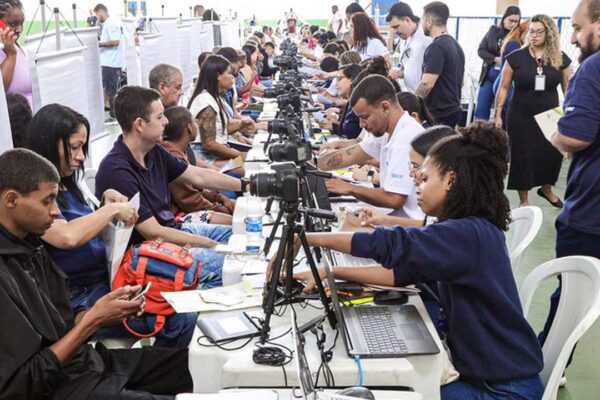 Profissionais trabalham em evento com câmeras, computadores e pessoas sentadas