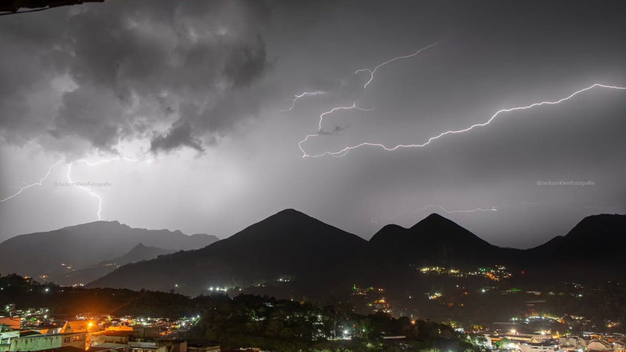 Relâmpagos iluminam o céu sobre montanhas e cidade durante tempestade em Nova Friburgo, RJ.