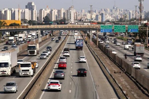 Rodovia com tráfego intenso e prédios ao fundo.
